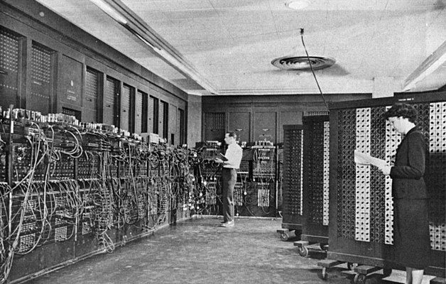 Historical photograph of a room-sized early electronic computer and an operator.